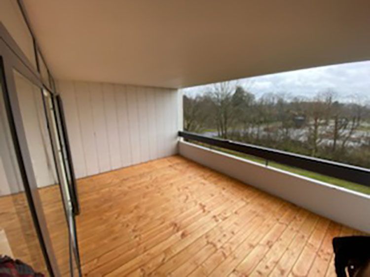 En balkon med trægulv og udsigt til træer.