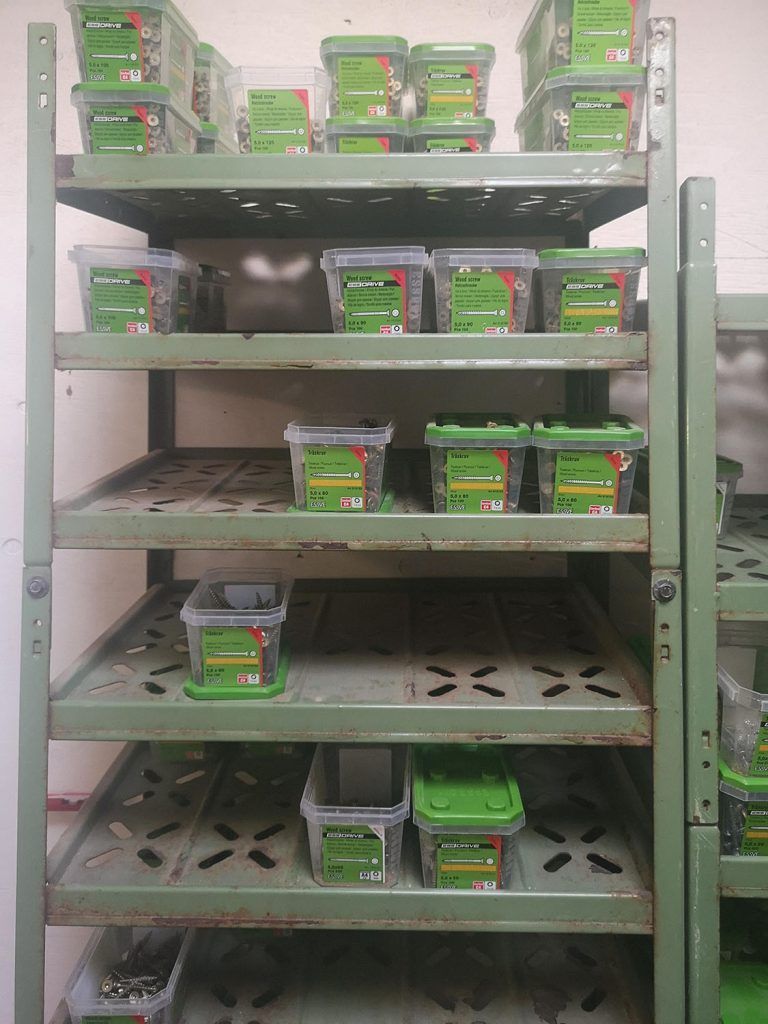 En hylde fyldt med grønne beholdere med møtrikker og bolte