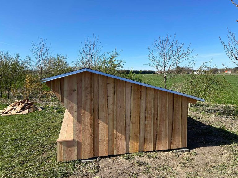 Et træskur med metaltag står midt på en græsmark.