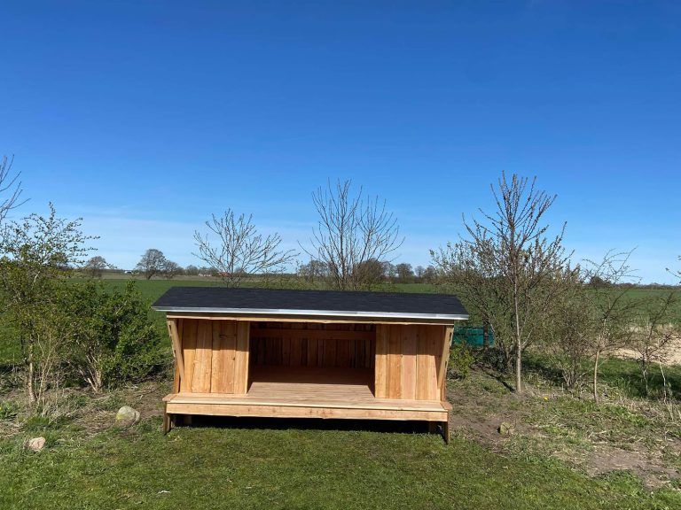 Midt på en græsmark står et lille træskjul.