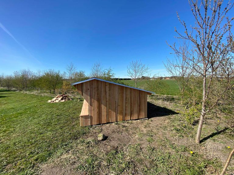 Et lille træskur står midt på en græsmark.