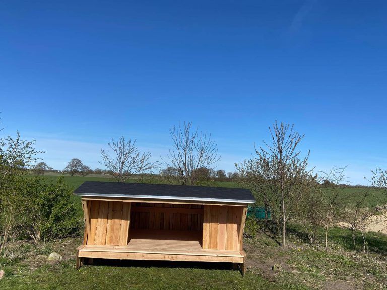 Midt på en græsmark står et lille træskjul.