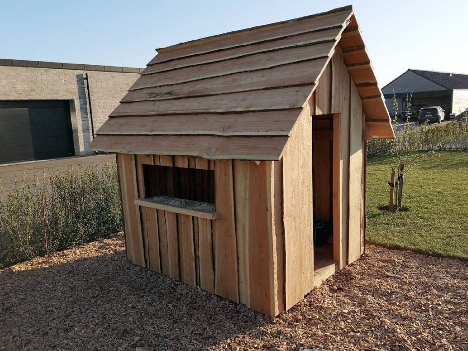 Et lille legehus i træ står midt på en frodig grøn mark.