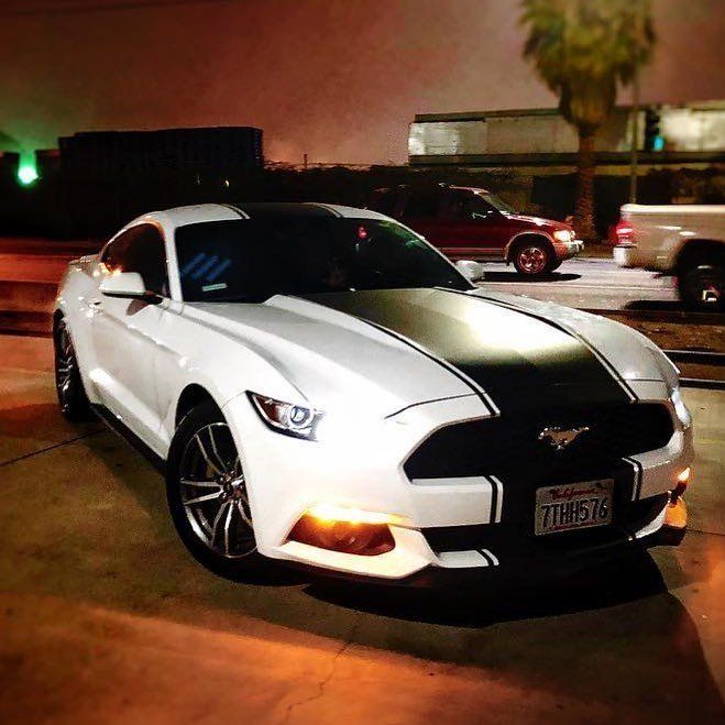 A white mustang is parked in a parking lot at night