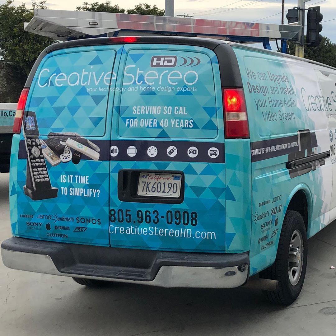 A blue and white van that says creative stereo on the back