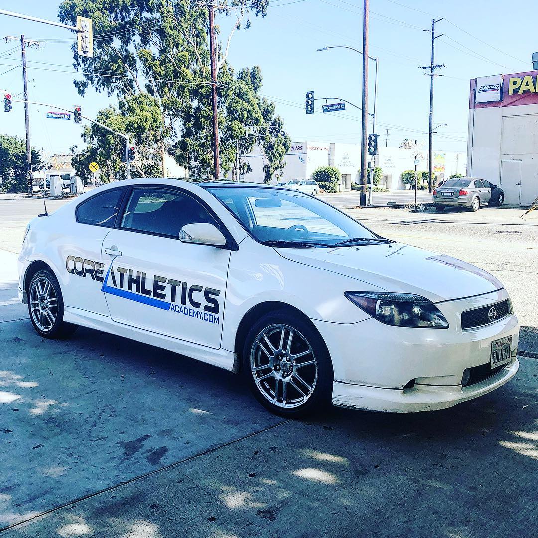 A white car with the word core athletics on the side is parked on the side of the road.