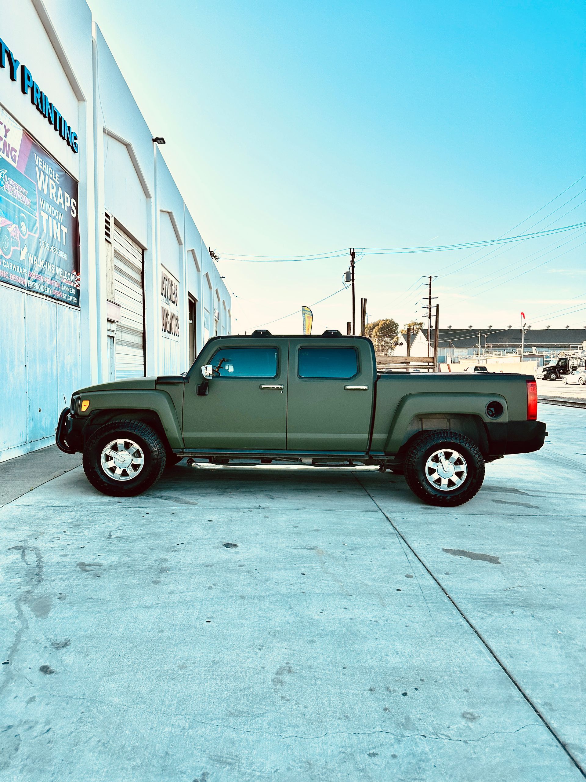 A green hummer truck is parked in front of a building.