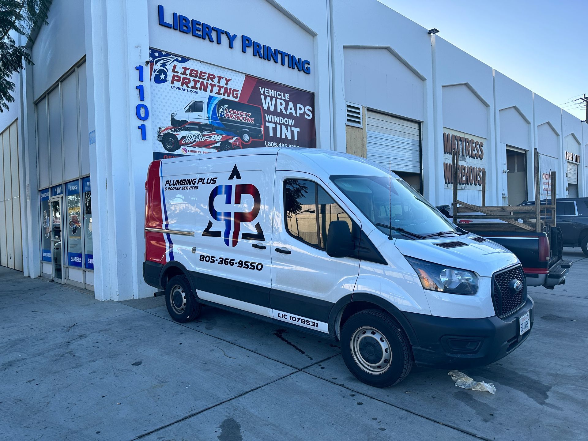 A white van is parked in front of a building that says liberty printing.