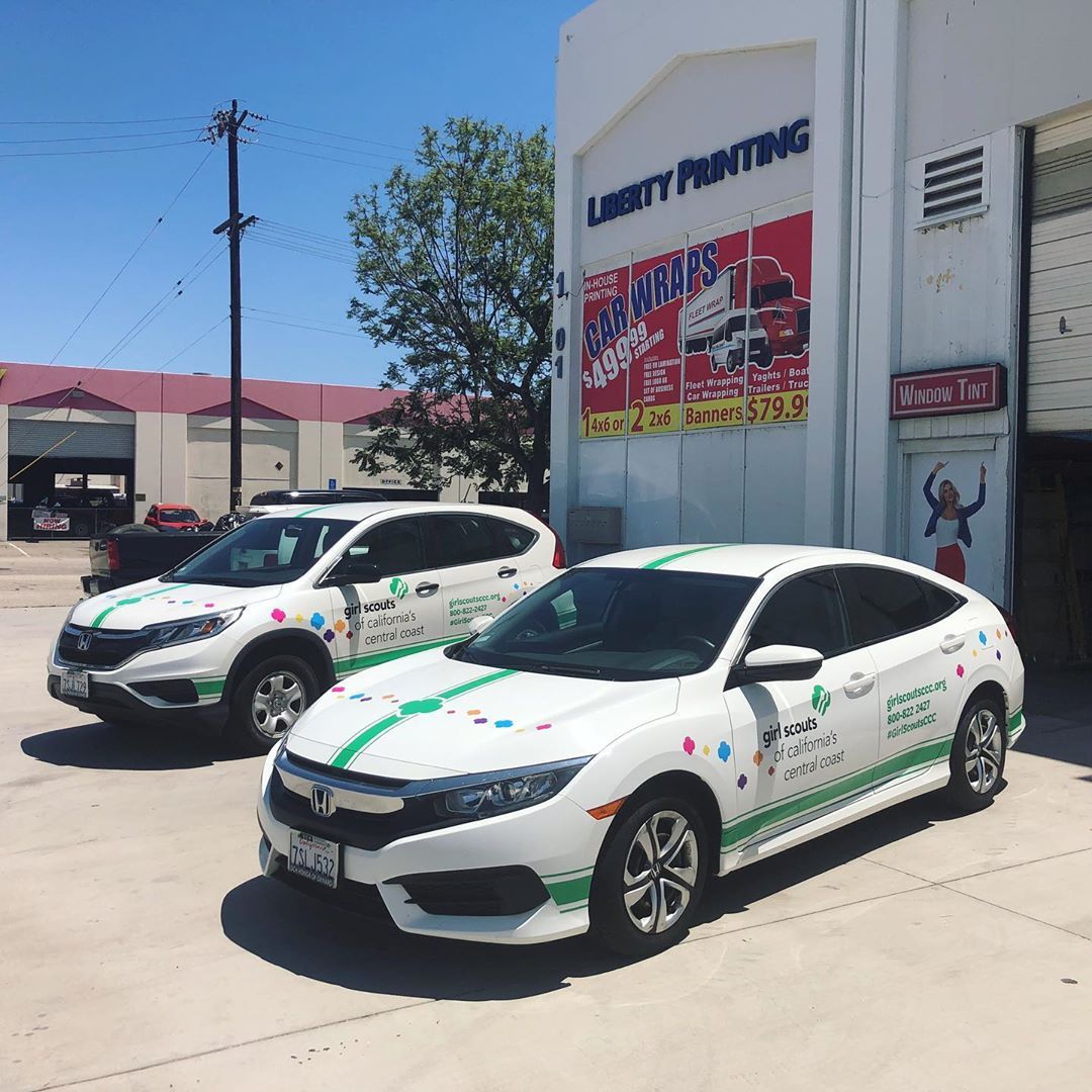 Two cars are parked in front of a building that says liberty printing