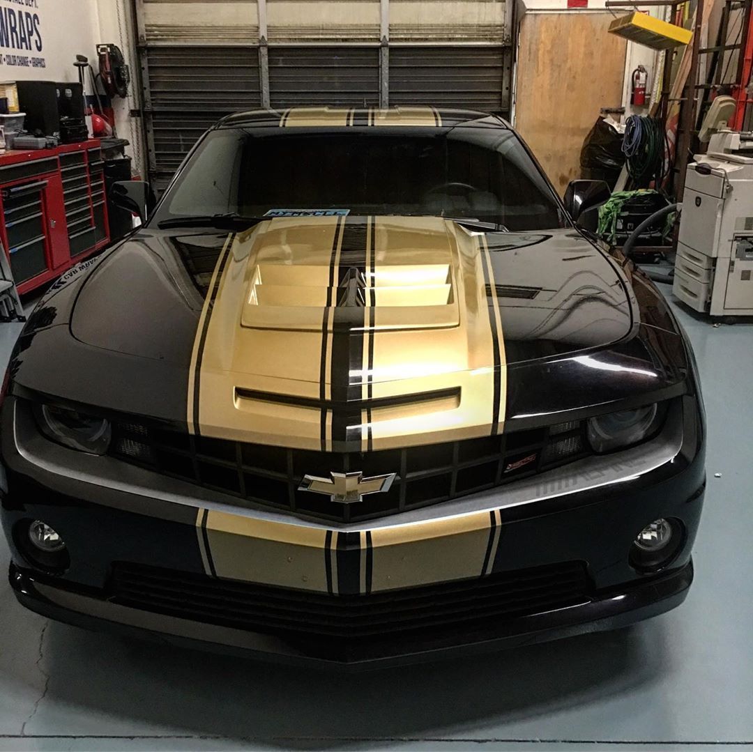A black car with gold stripes on the hood is parked in a garage.