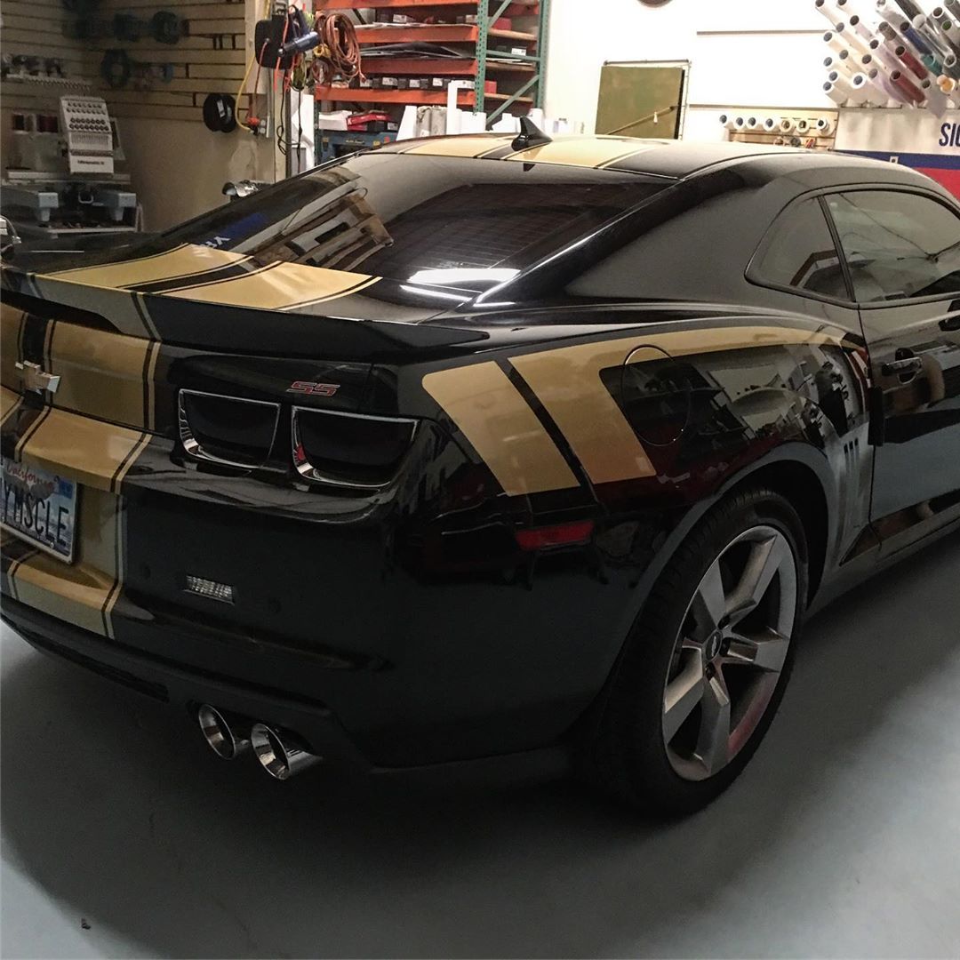 A black car with yellow stripes is parked in a garage