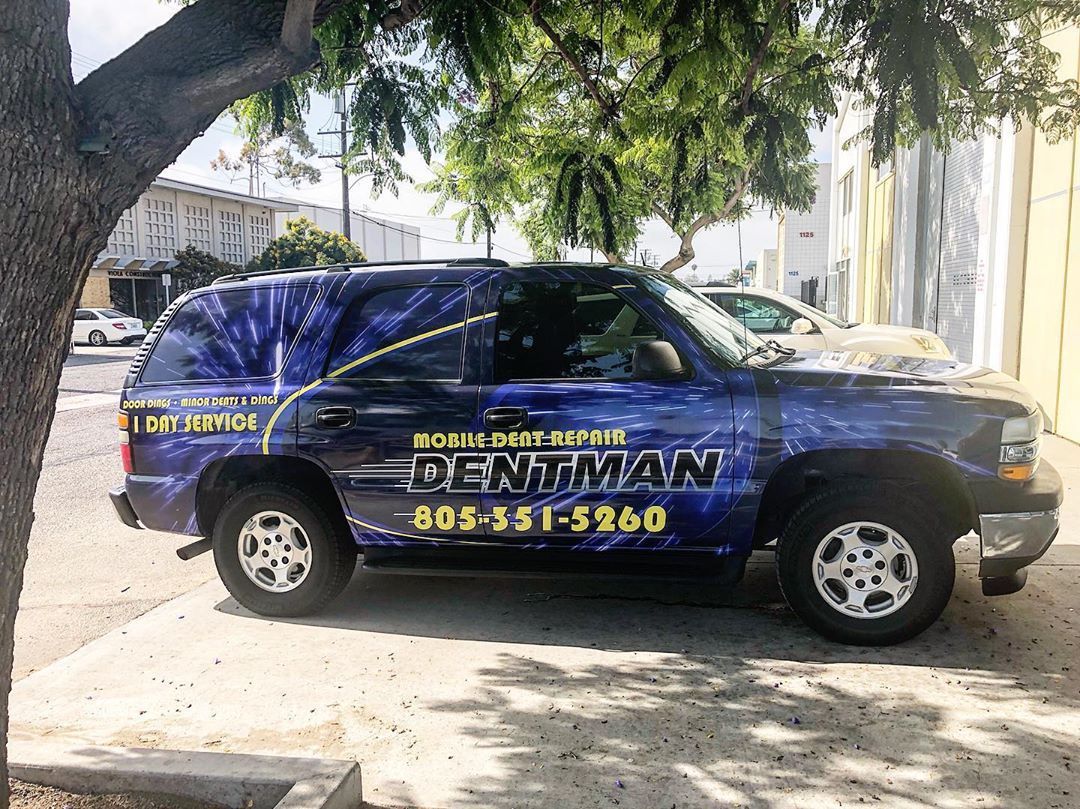 A blue rentman truck is parked in a parking lot next to a tree.