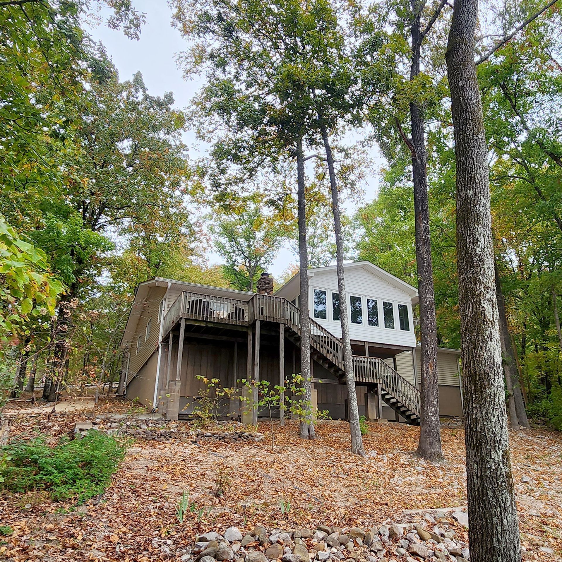 House nestled among trees; weathered wooden deck and stairs. Fall foliage.