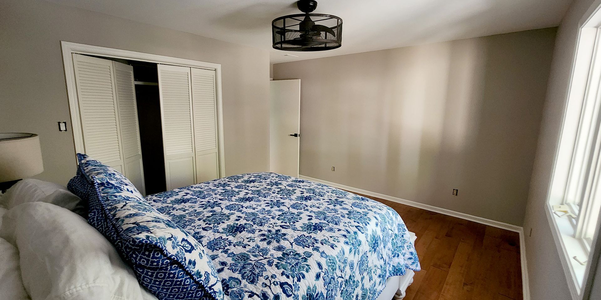 Bedroom with bed, blue and white floral bedding, closet, ceiling fan, and window.