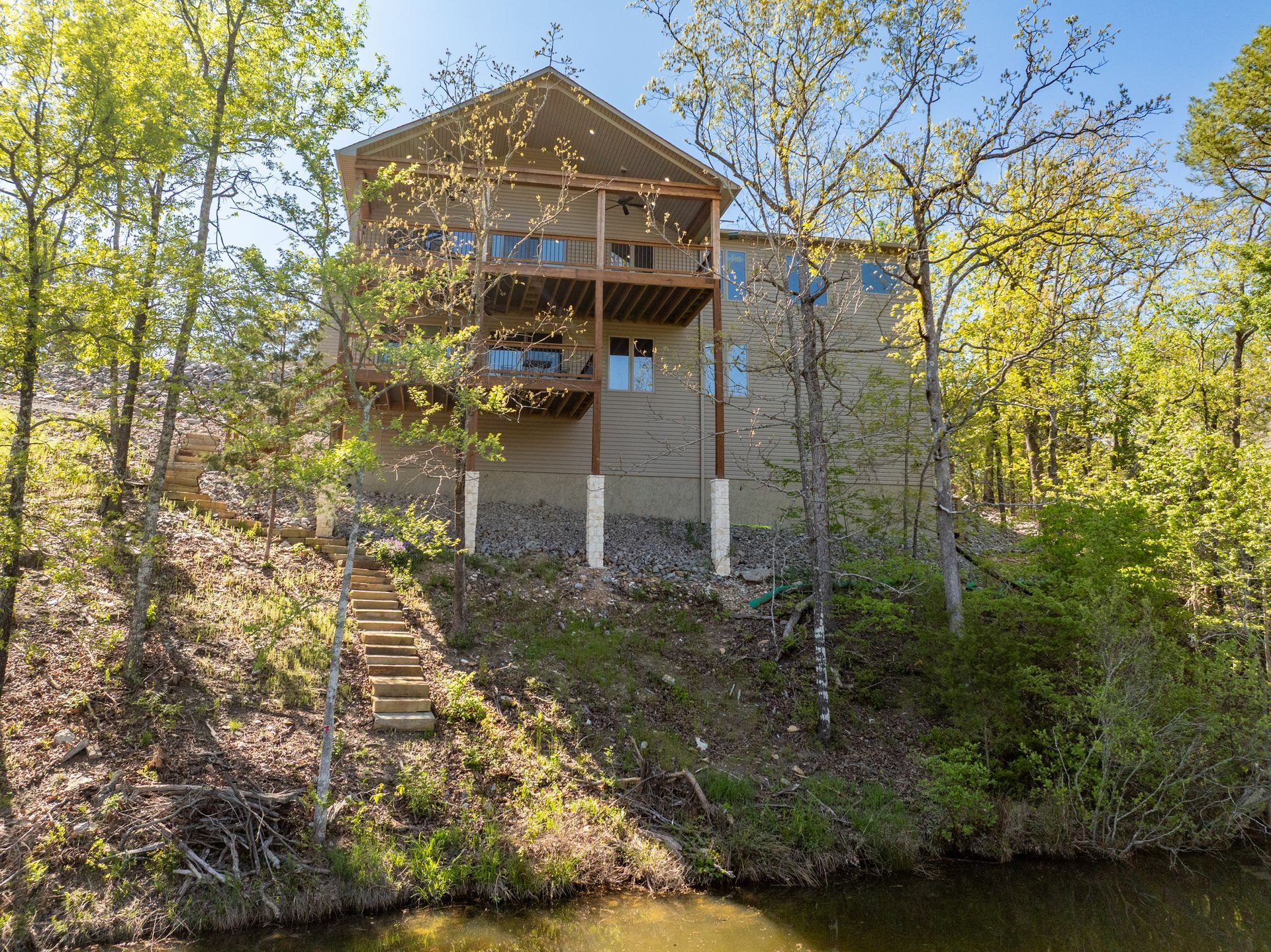 A large house is sitting on top of a hill next to a lake surrounded by trees.