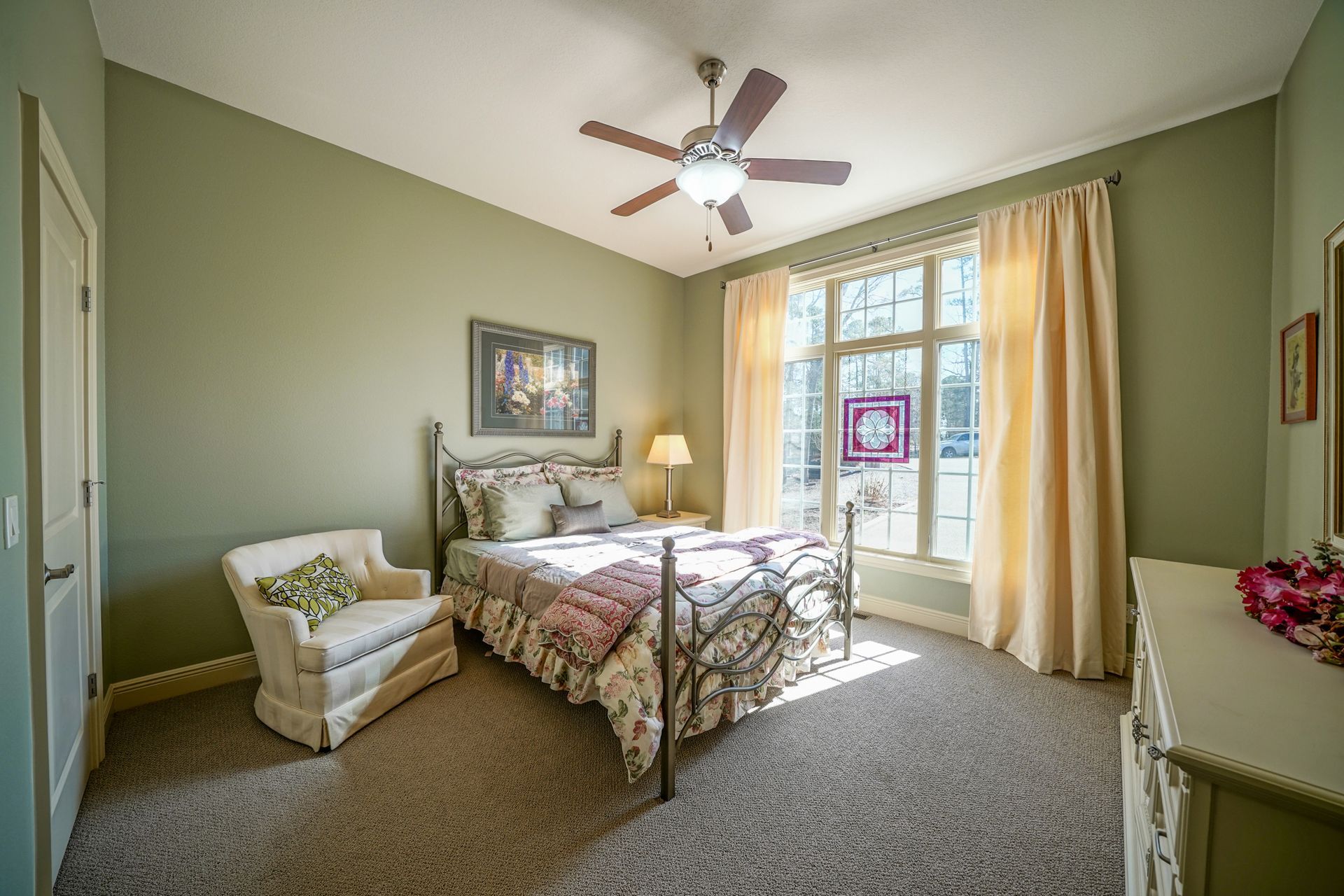 A bedroom with a bed , chair , dresser and ceiling fan.