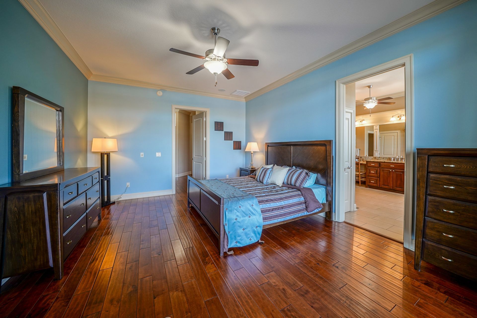 A bedroom with a bed , dresser , mirror and ceiling fan.