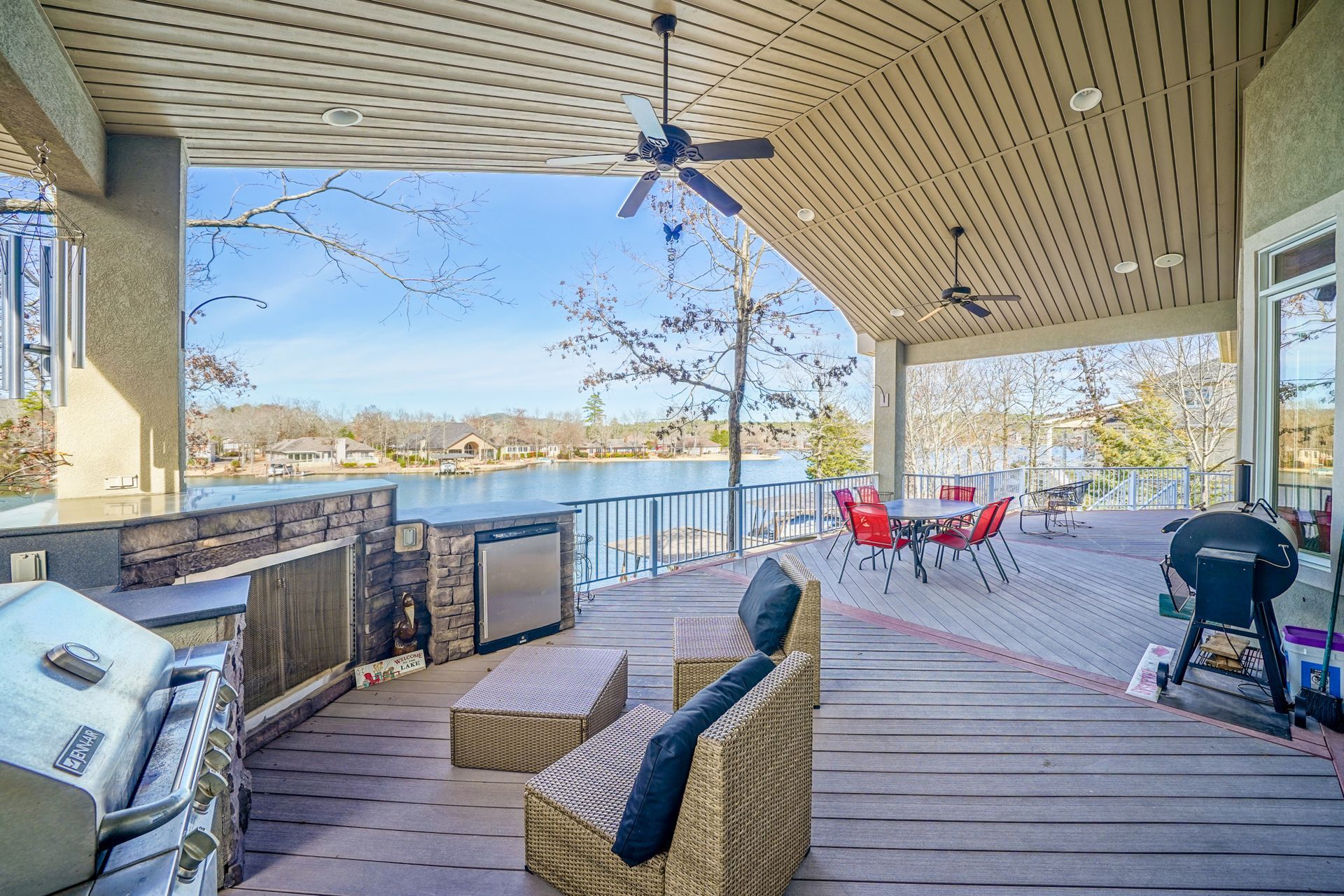 A large covered deck with a grill , chairs , tables and a view of a lake.