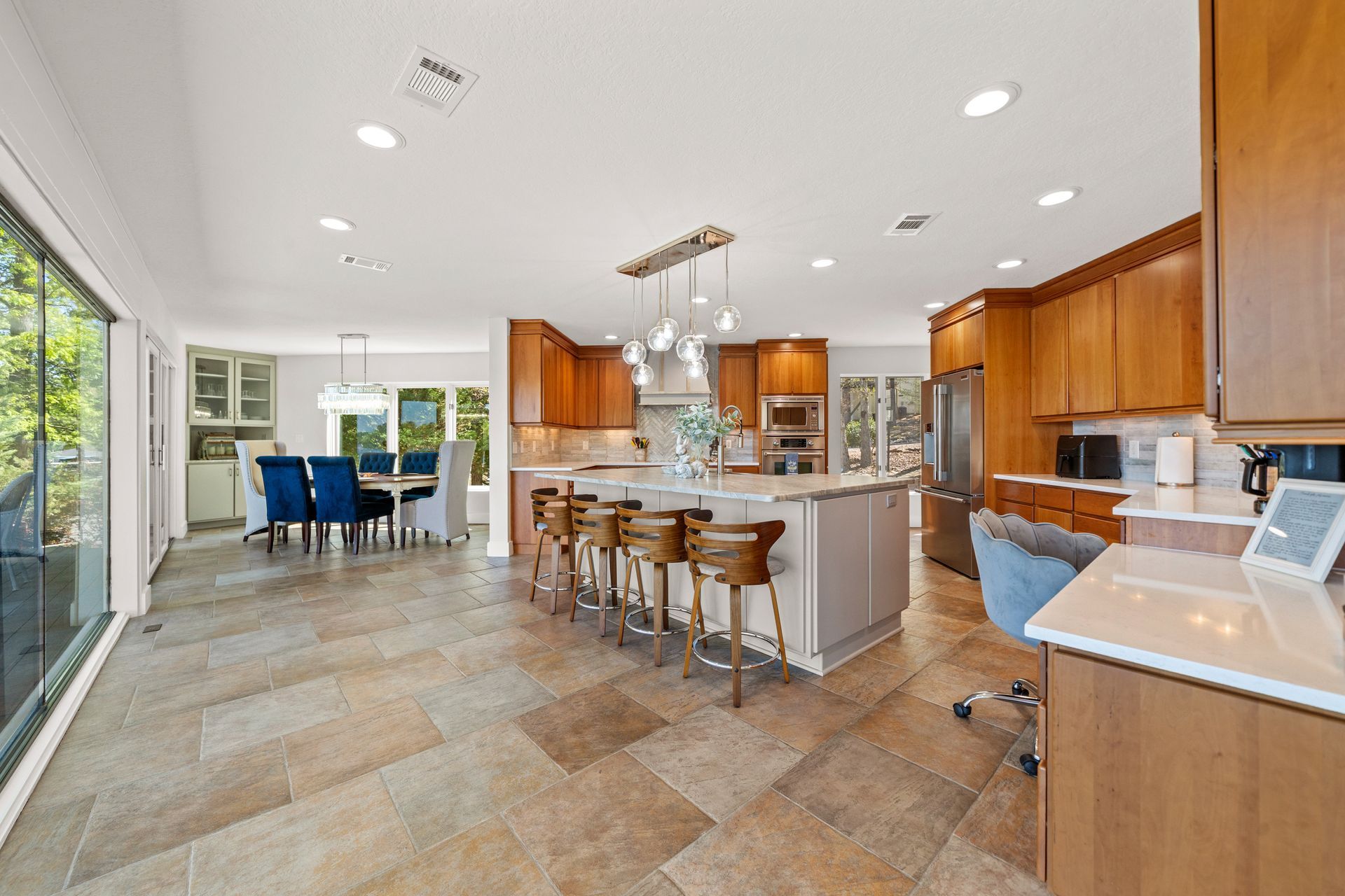 A kitchen with a large island and stools and a dining room in the background.