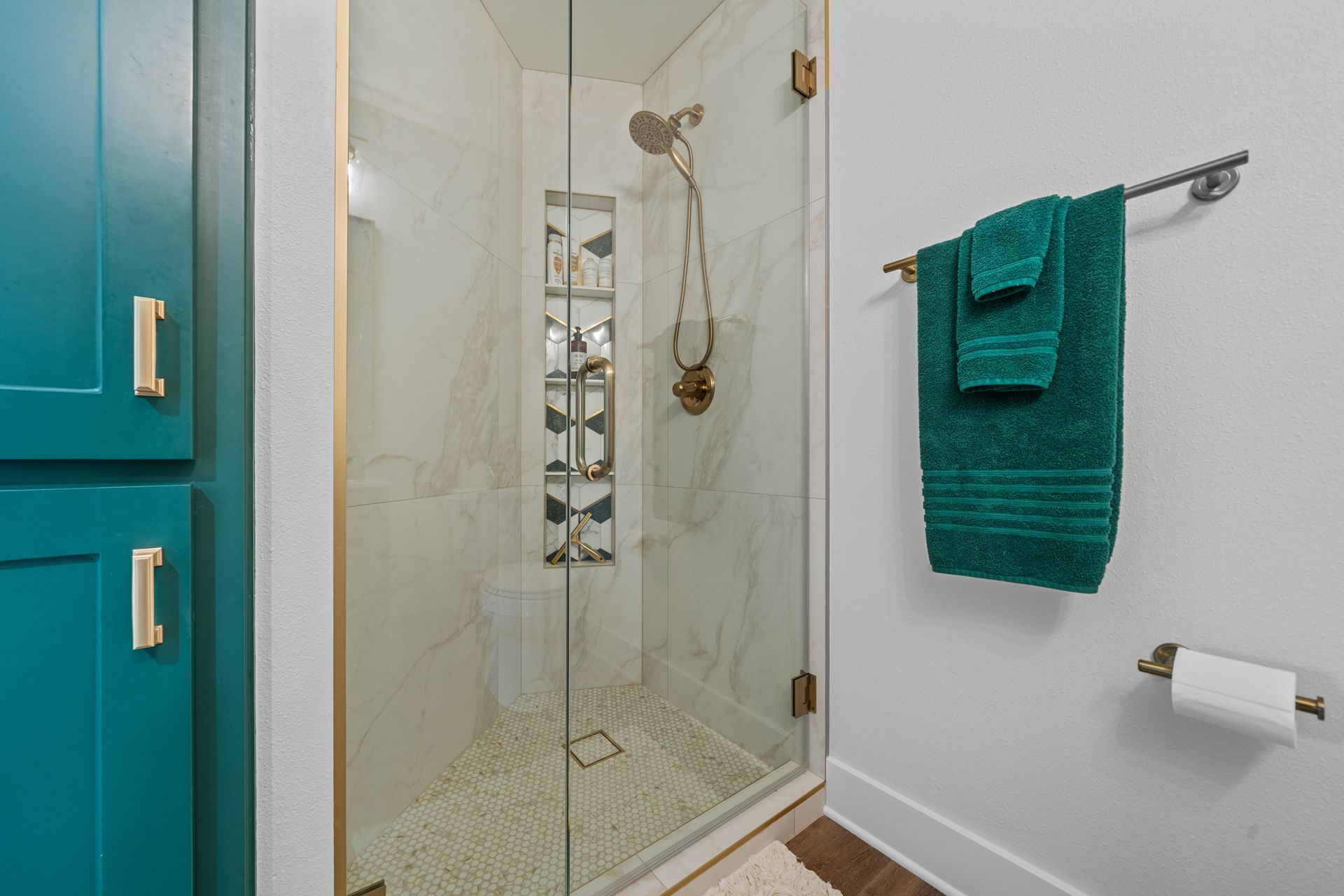 A bathroom with a walk in shower and green towels hanging on the wall.