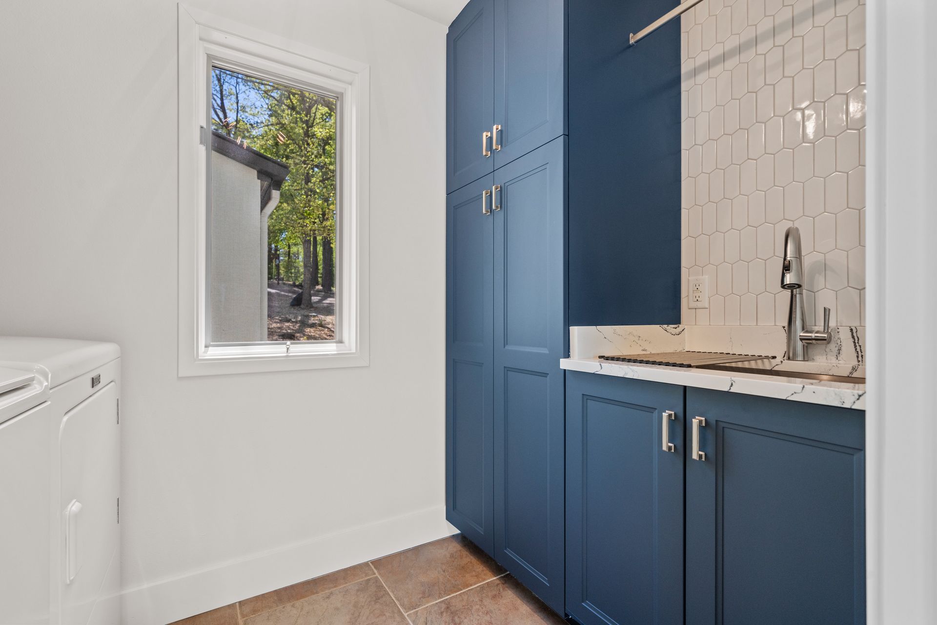 A laundry room with blue cabinets , a sink , and a window.