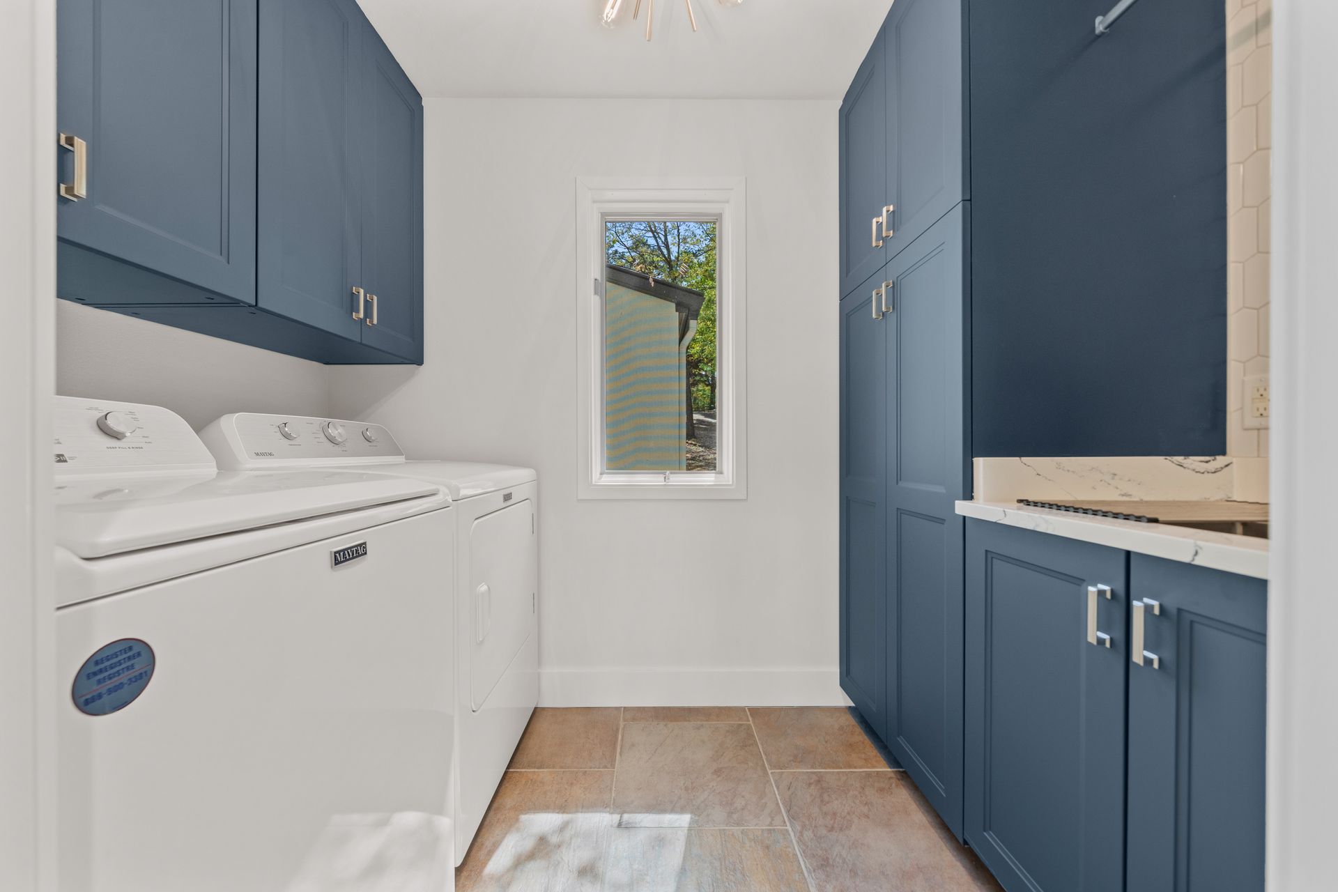A laundry room with blue cabinets , a washer and dryer , and a window.