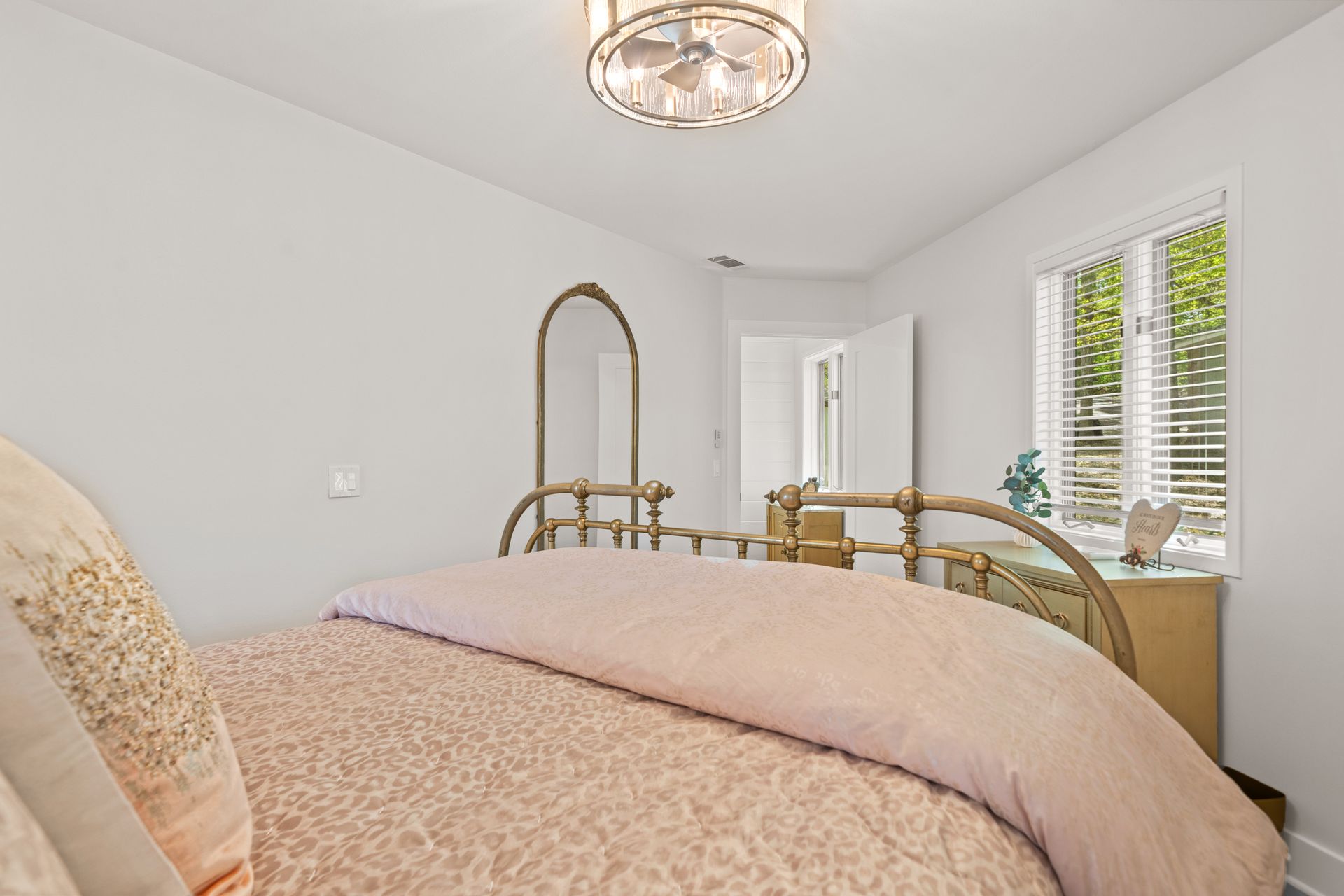A bedroom with a bed , dresser , mirror and window.
