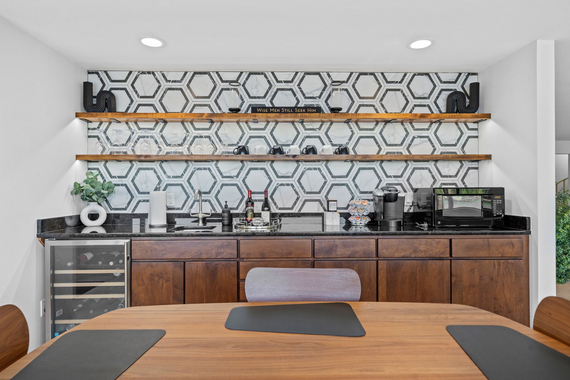 A dining room with a table , chairs , shelves and a wine cooler.