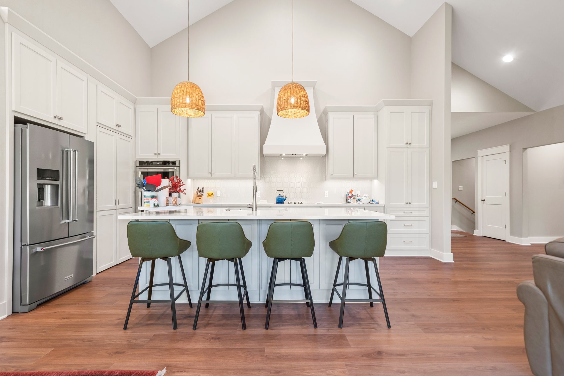A kitchen with white cabinets , stainless steel appliances , a large island , and green stools.