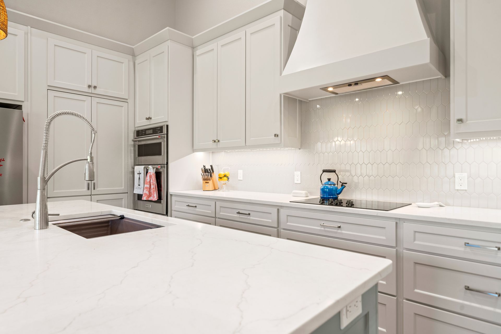 A kitchen with white cabinets , white counter tops , a sink , and a stove.