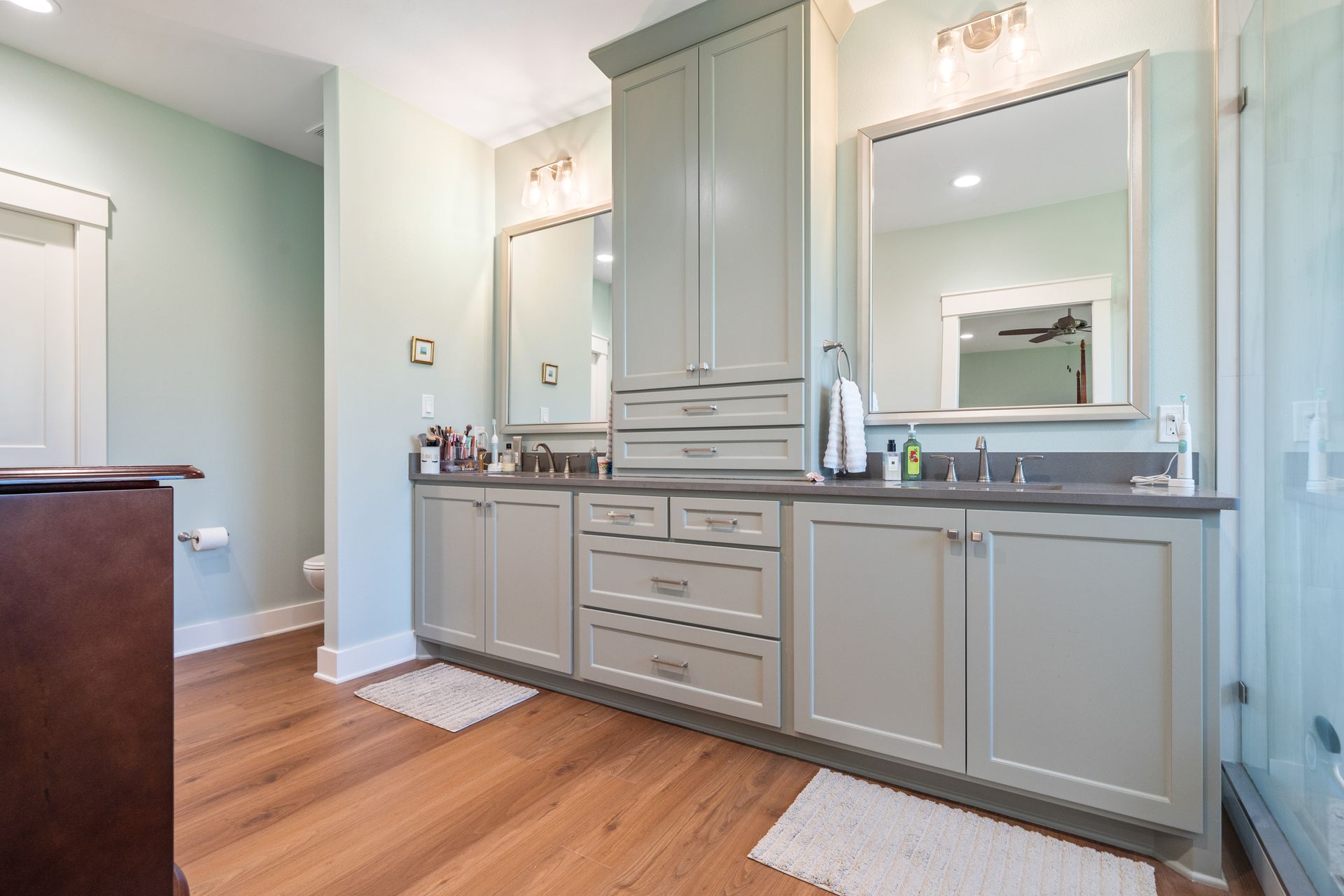 A bathroom with two sinks , two mirrors , and hardwood floors.