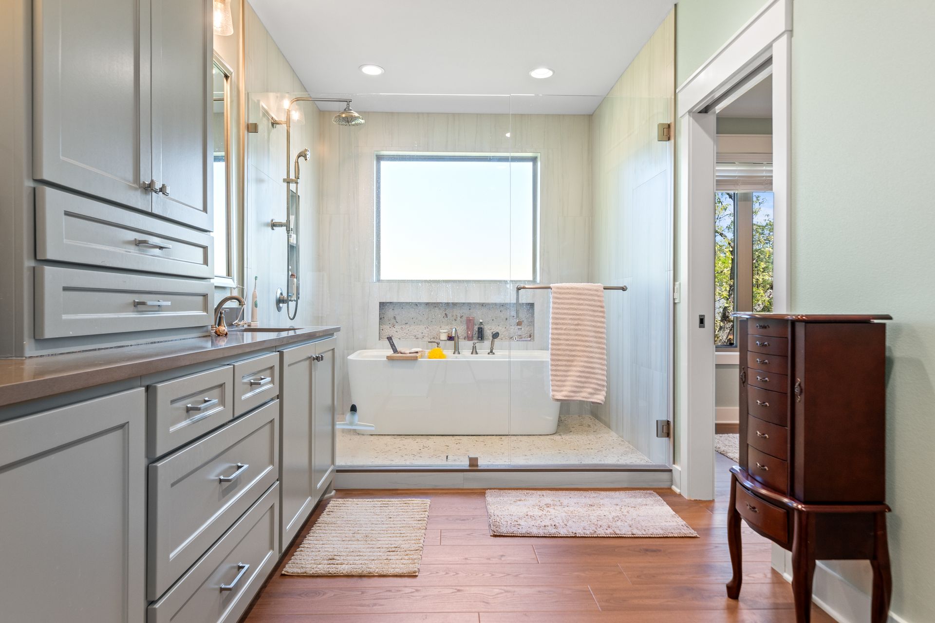 A bathroom with a tub , sink , cabinets and a window.