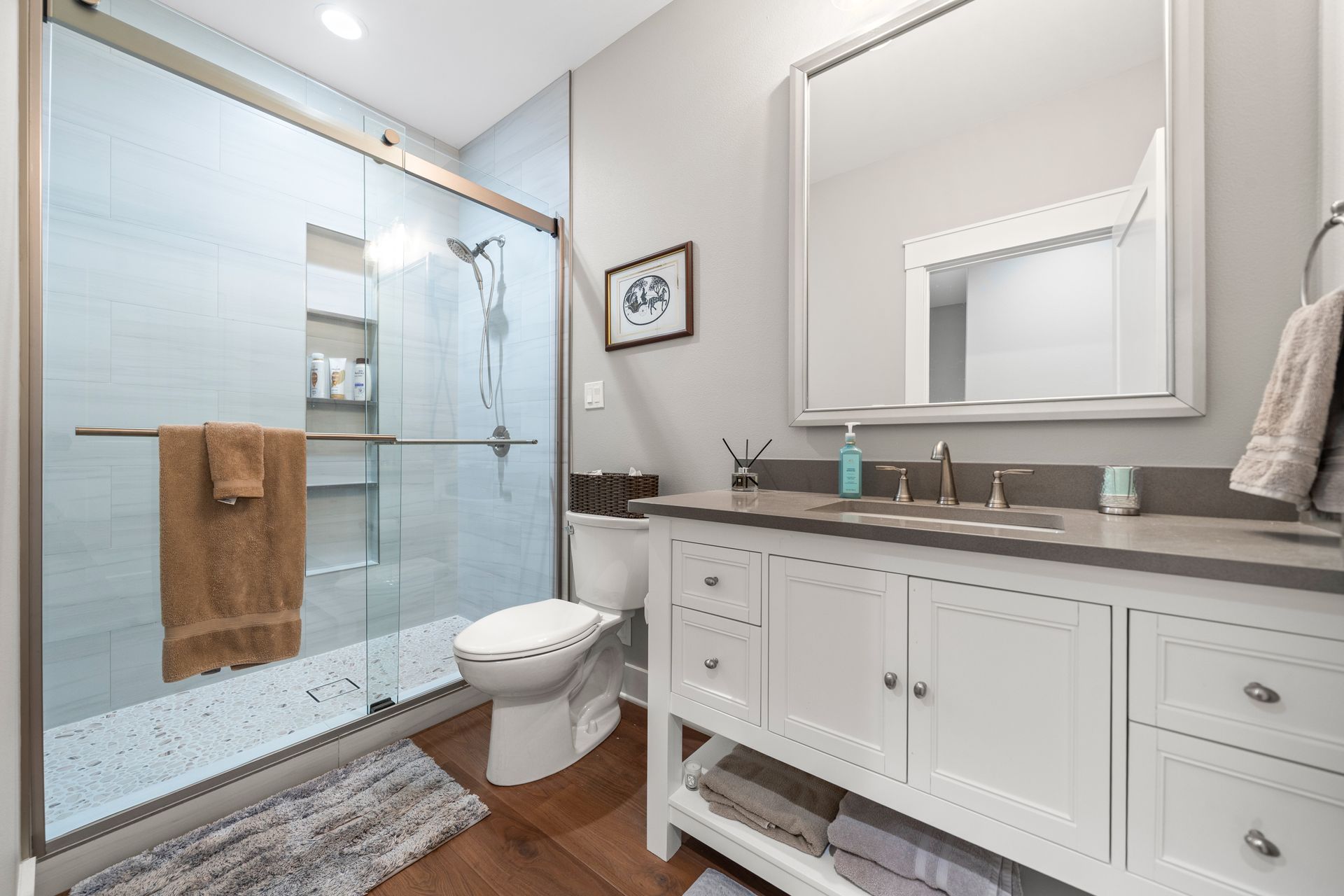 A bathroom with a toilet , sink , mirror and walk in shower.