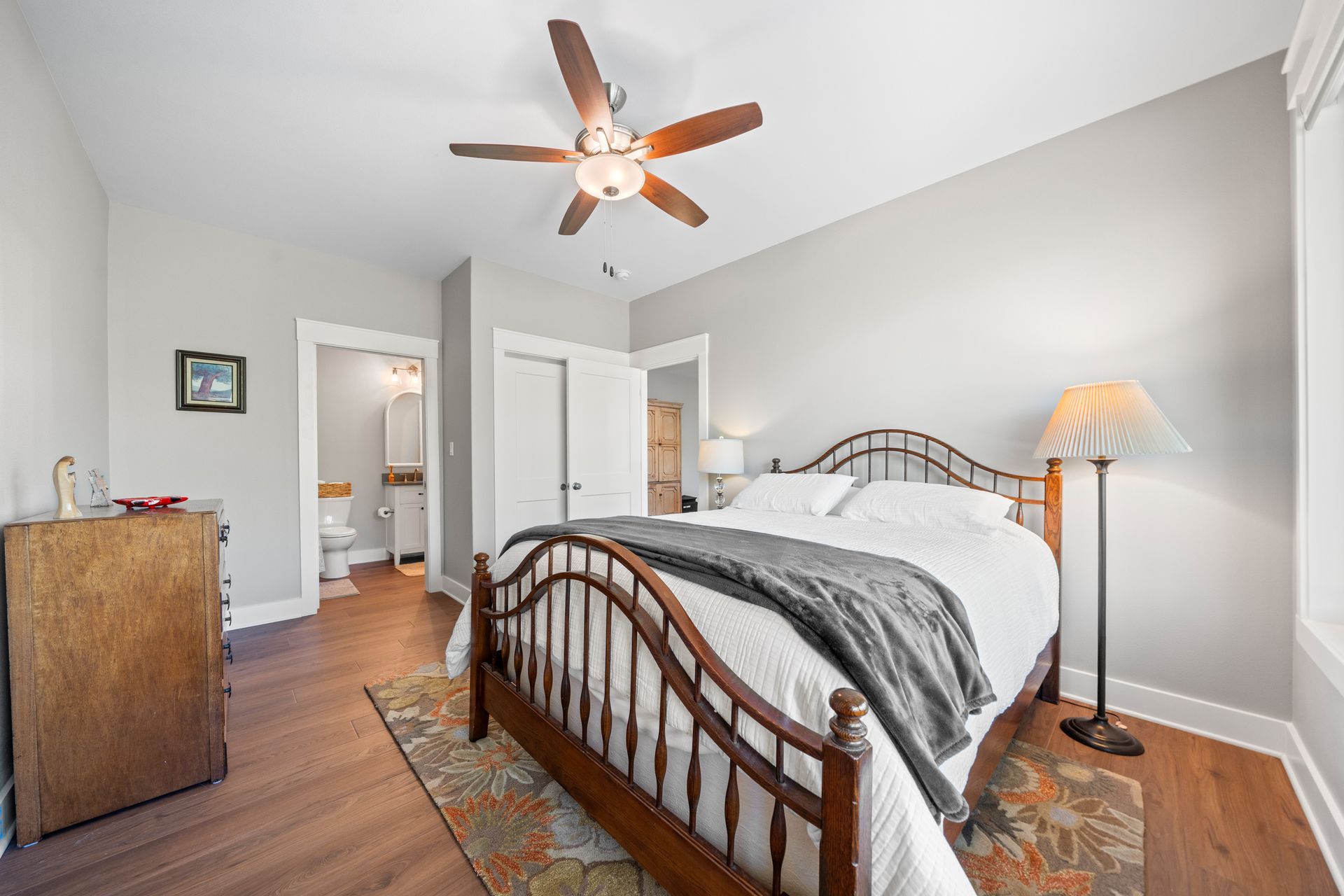 A bedroom with a bed , ceiling fan , lamp and dresser.