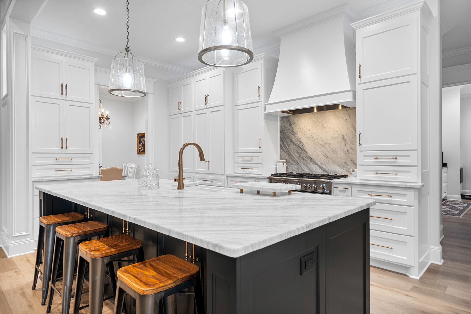 A kitchen with white cabinets , granite counter tops , stools and a large island.