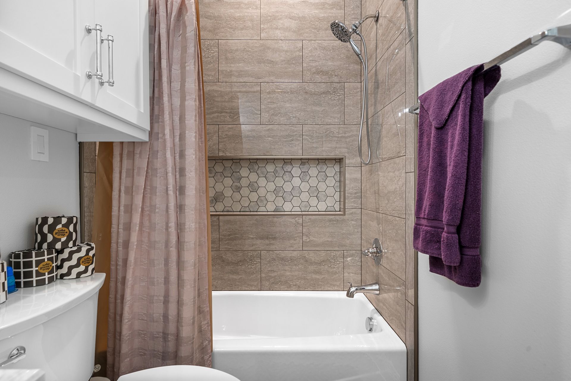A bathroom with a tub , toilet , shower and purple towel hanging on the wall.