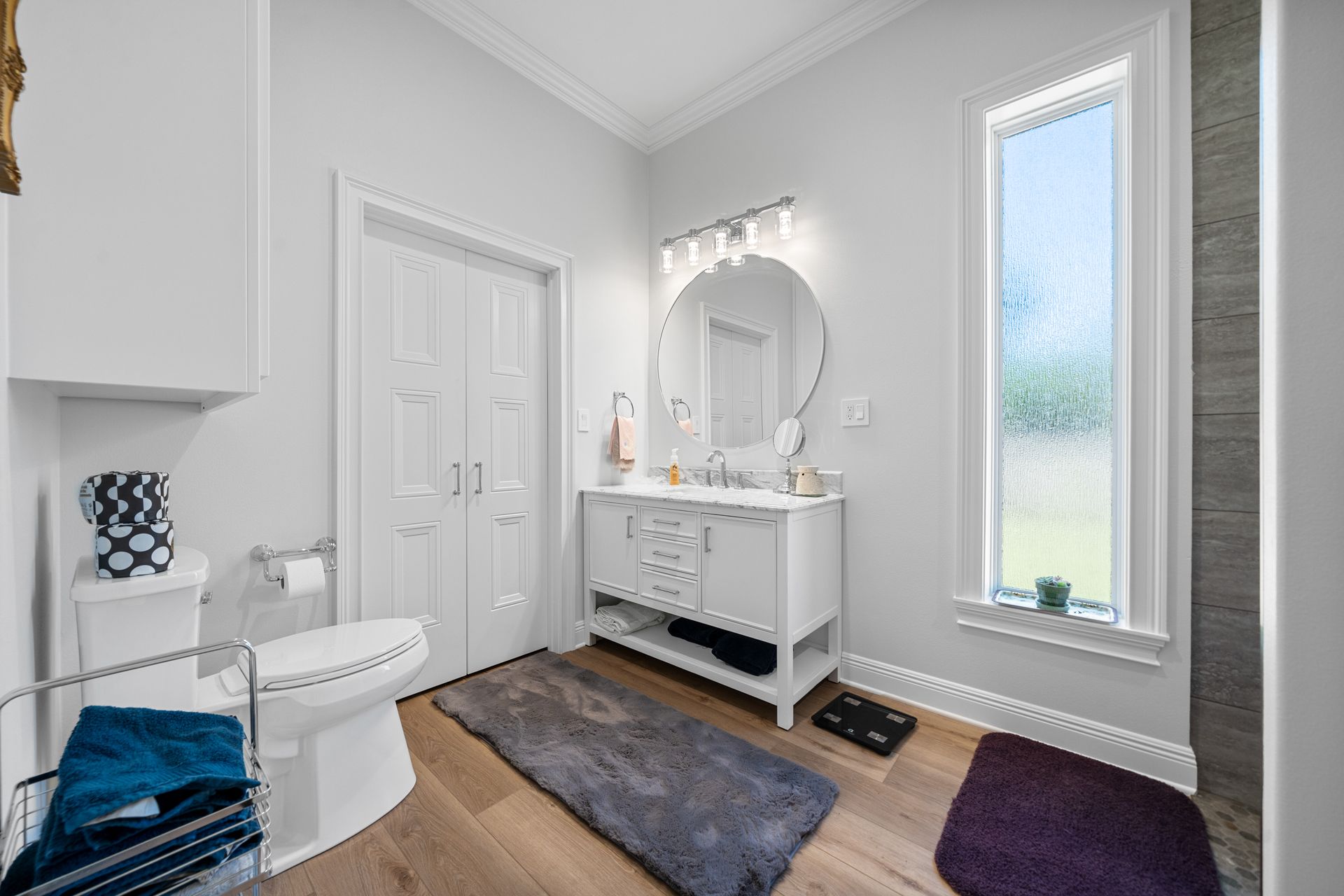 A bathroom with a toilet , sink , mirror and window.
