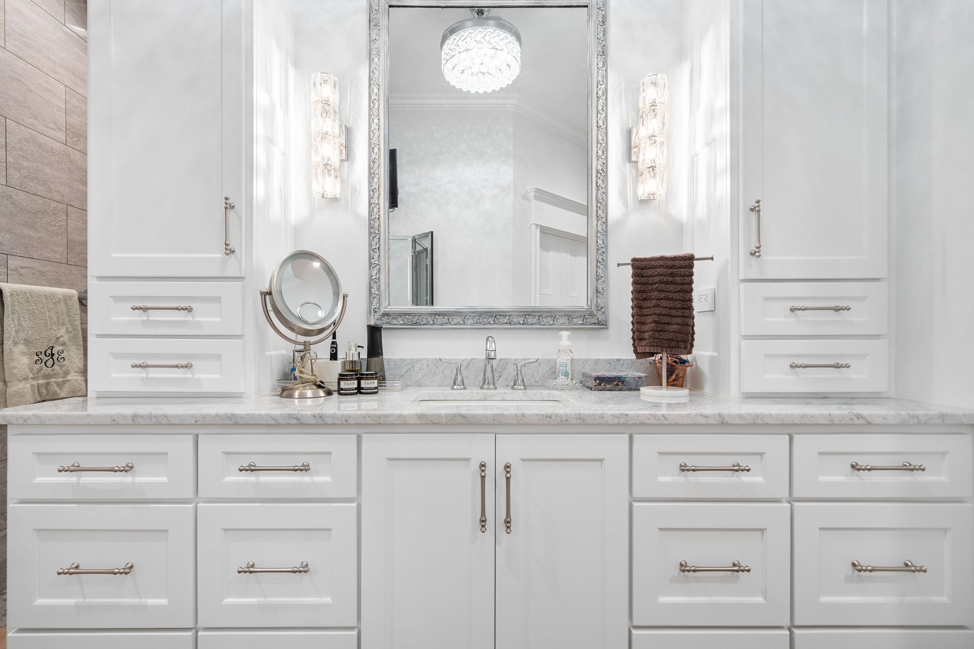 A bathroom with white cabinets , drawers , a sink and a mirror.
