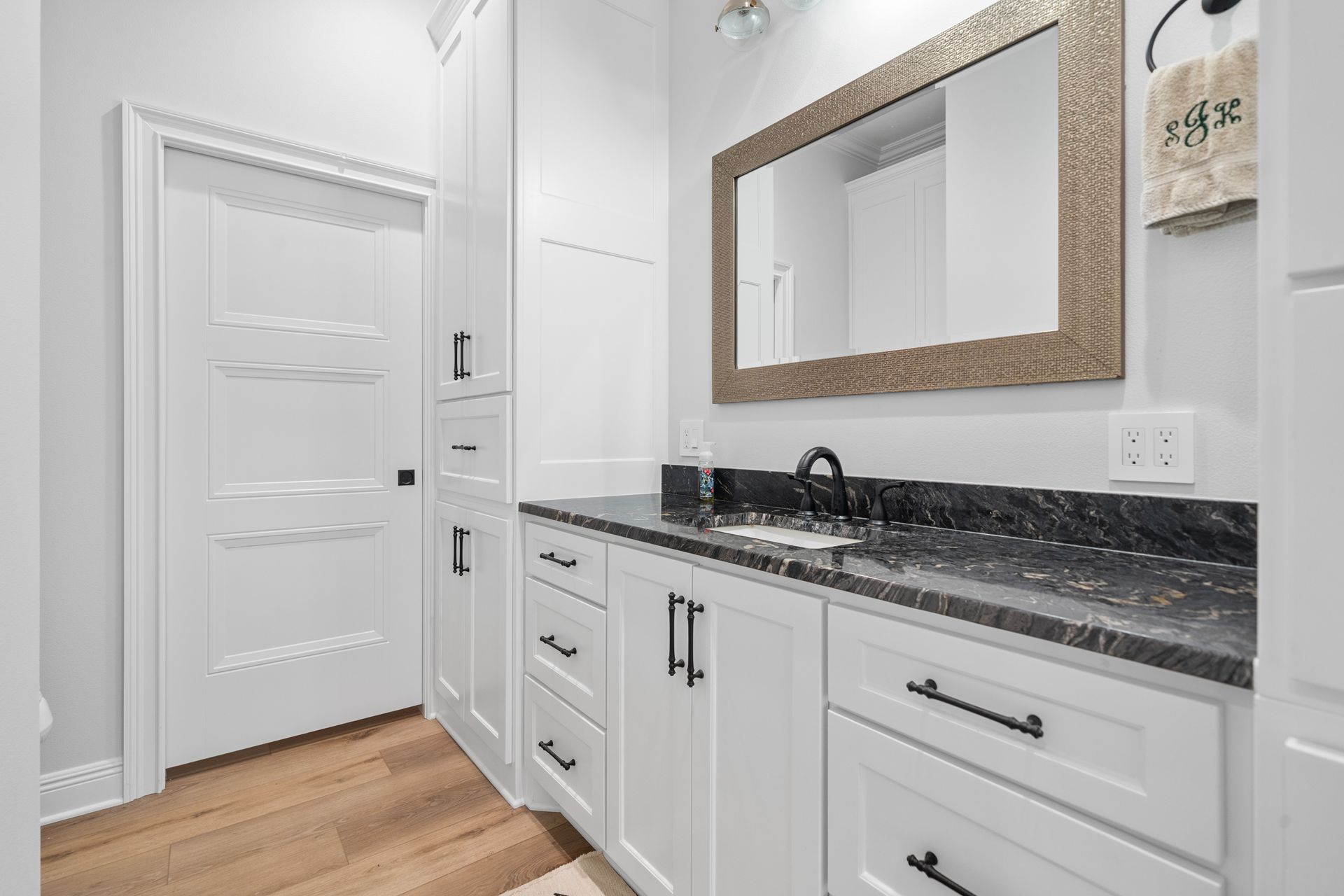 A bathroom with white cabinets , black counter tops , a sink and a mirror.