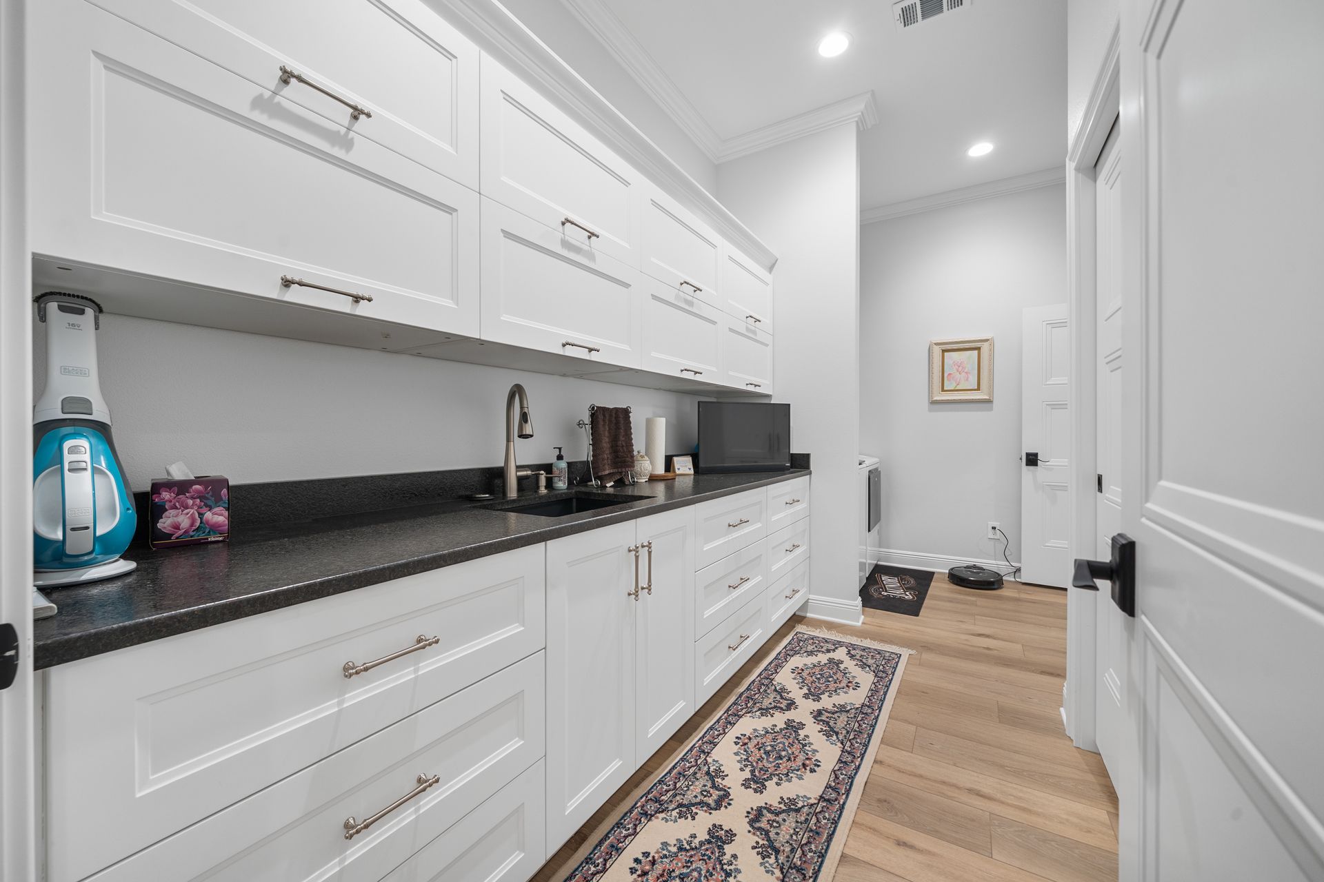 A kitchen with white cabinets and black counter tops and a rug on the floor.