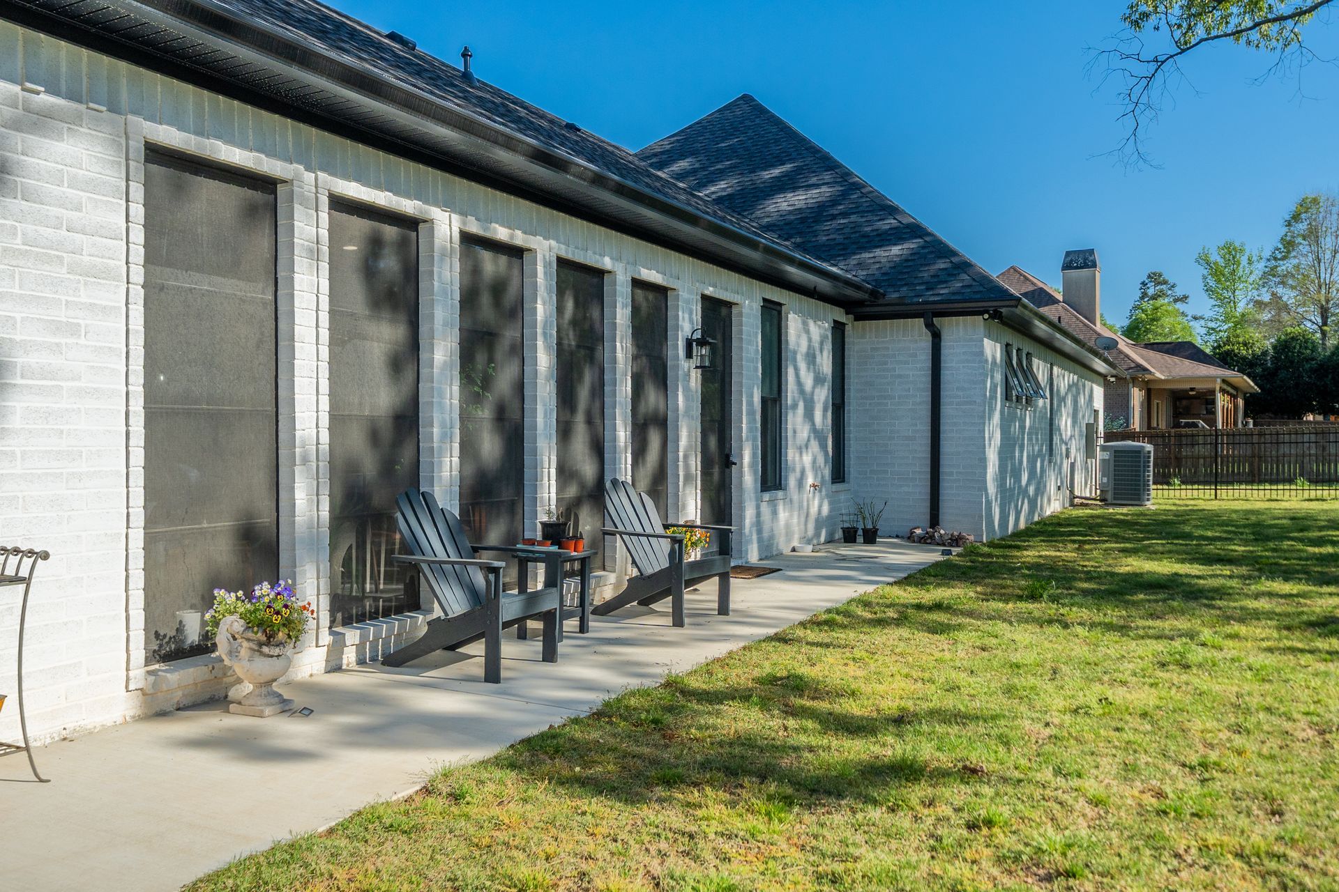 A white brick house with a screened in porch and chairs in front of it.