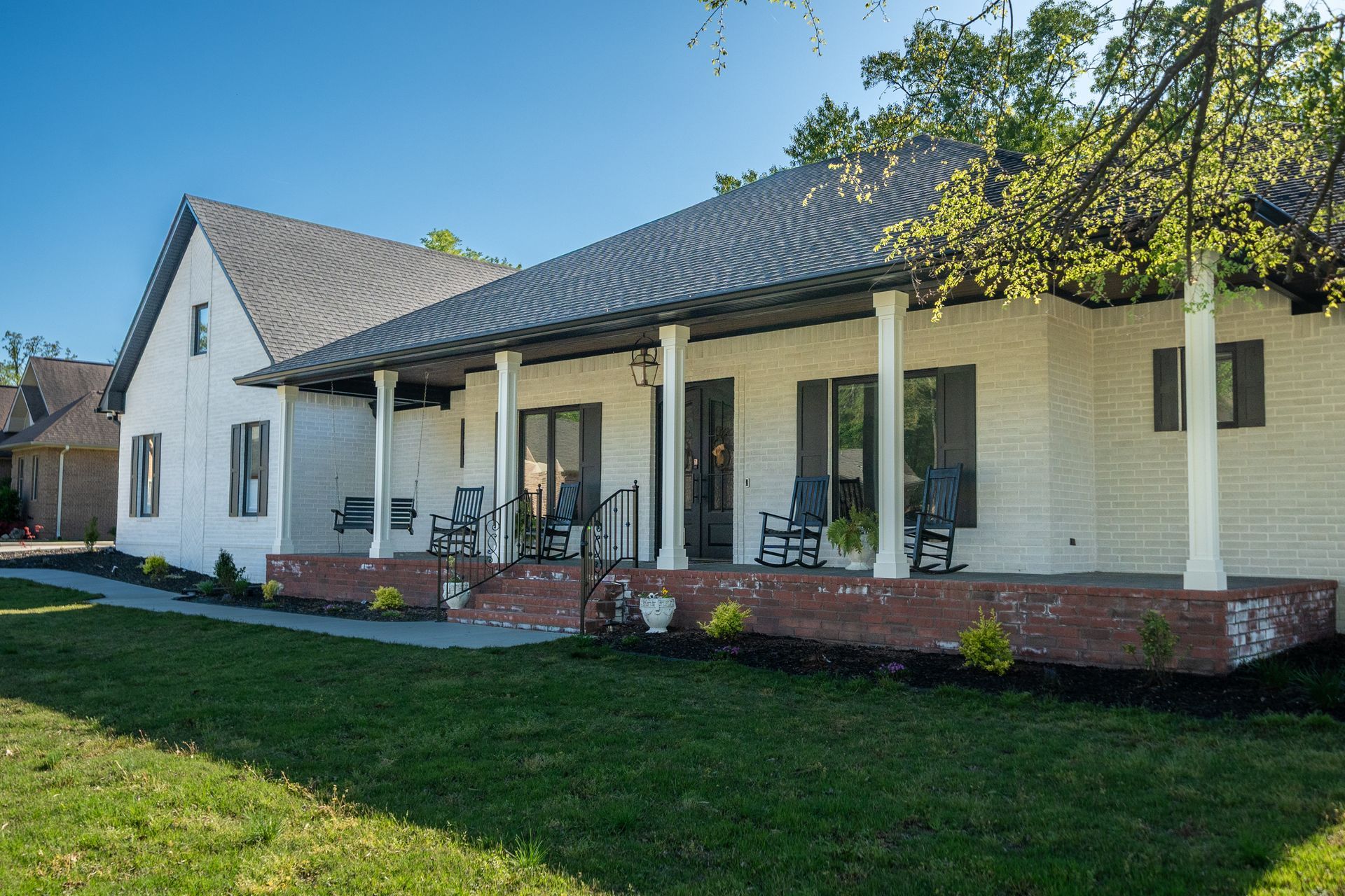 A white house with a large porch and rocking chairs on it.