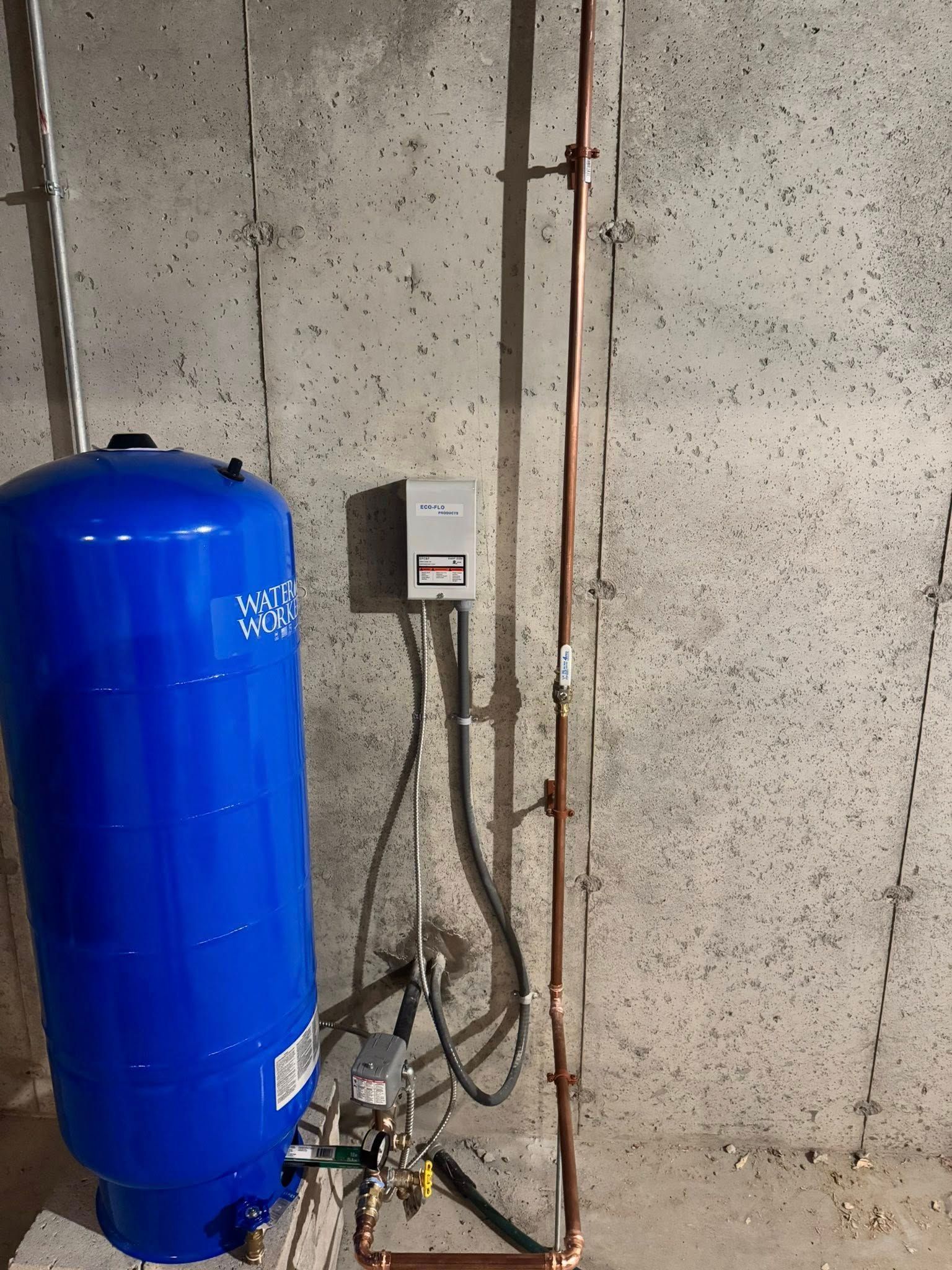 A water heater is sitting in a room next to a brick wall.