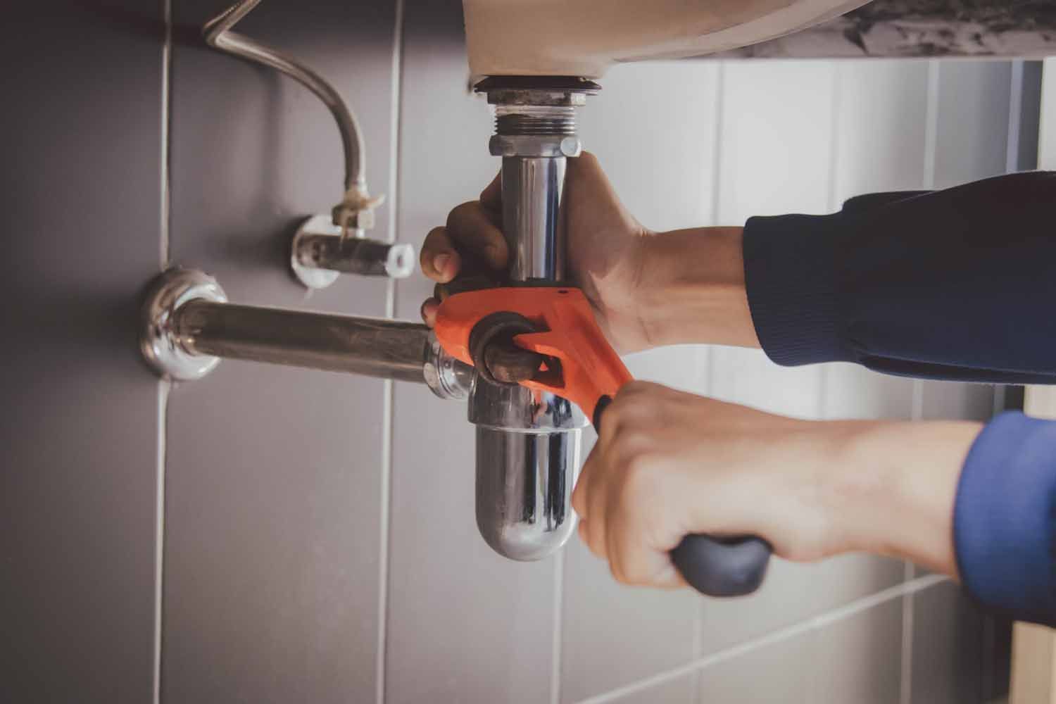 A plumber is fixing a sink pipe with a wrench.