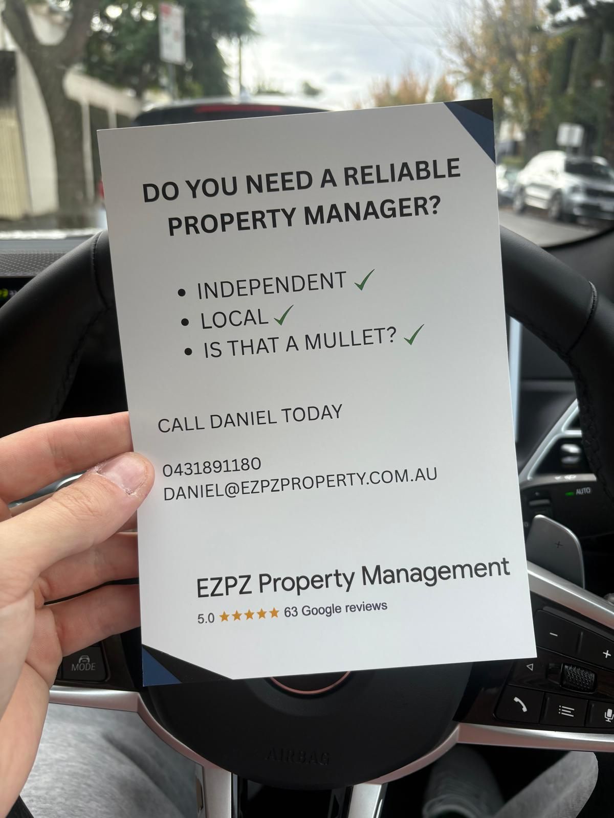A flyer held in a person's hand inside a car, advertising a property manager. It reads 