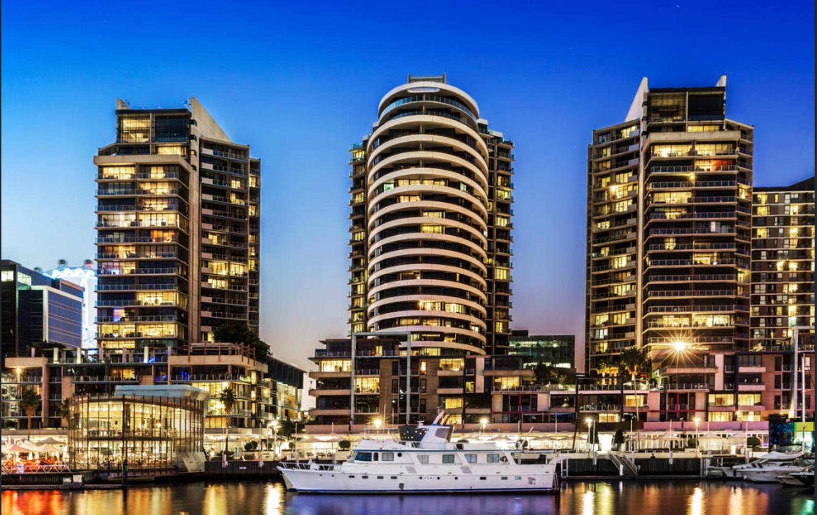 Buildings at night over water; illuminated windows, white boat, dark sky.