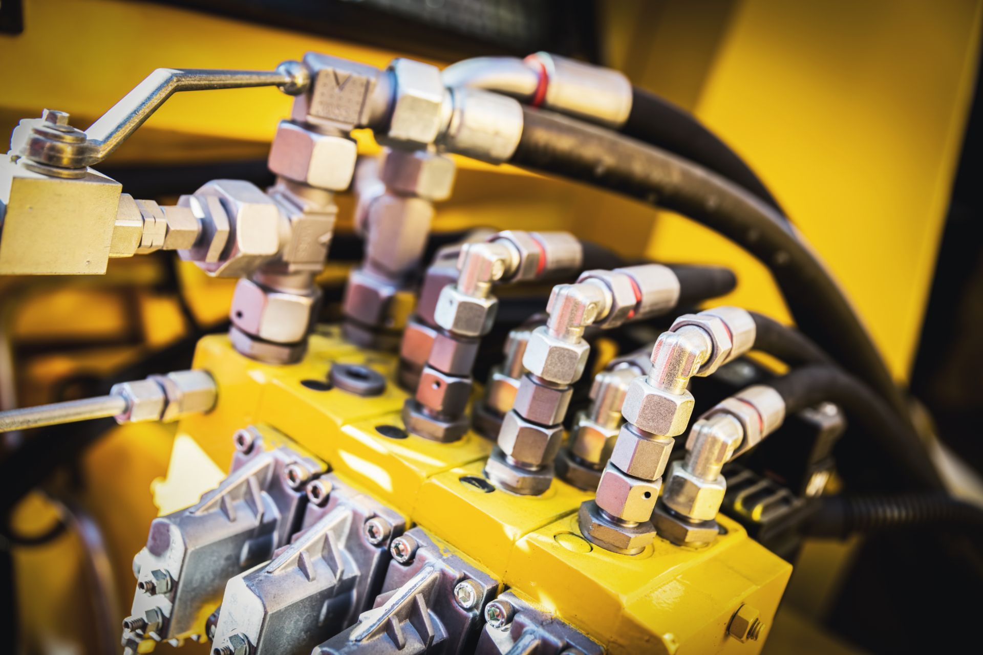 A close up of hydraulic hoses and valves on a yellow machine.