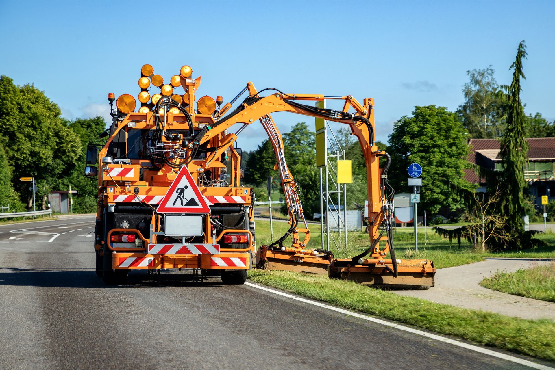 A truck is cutting grass on the side of the road.