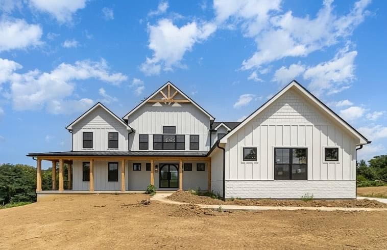 A large white house with black windows is sitting on top of a dirt field.