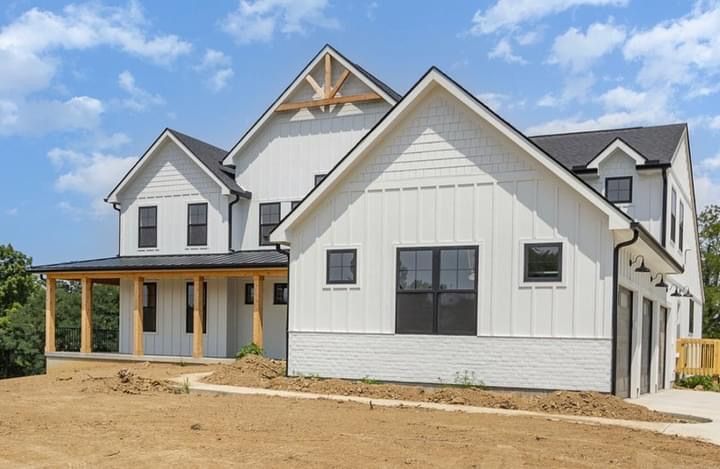 A large white house with a black roof is sitting on top of a dirt hill.